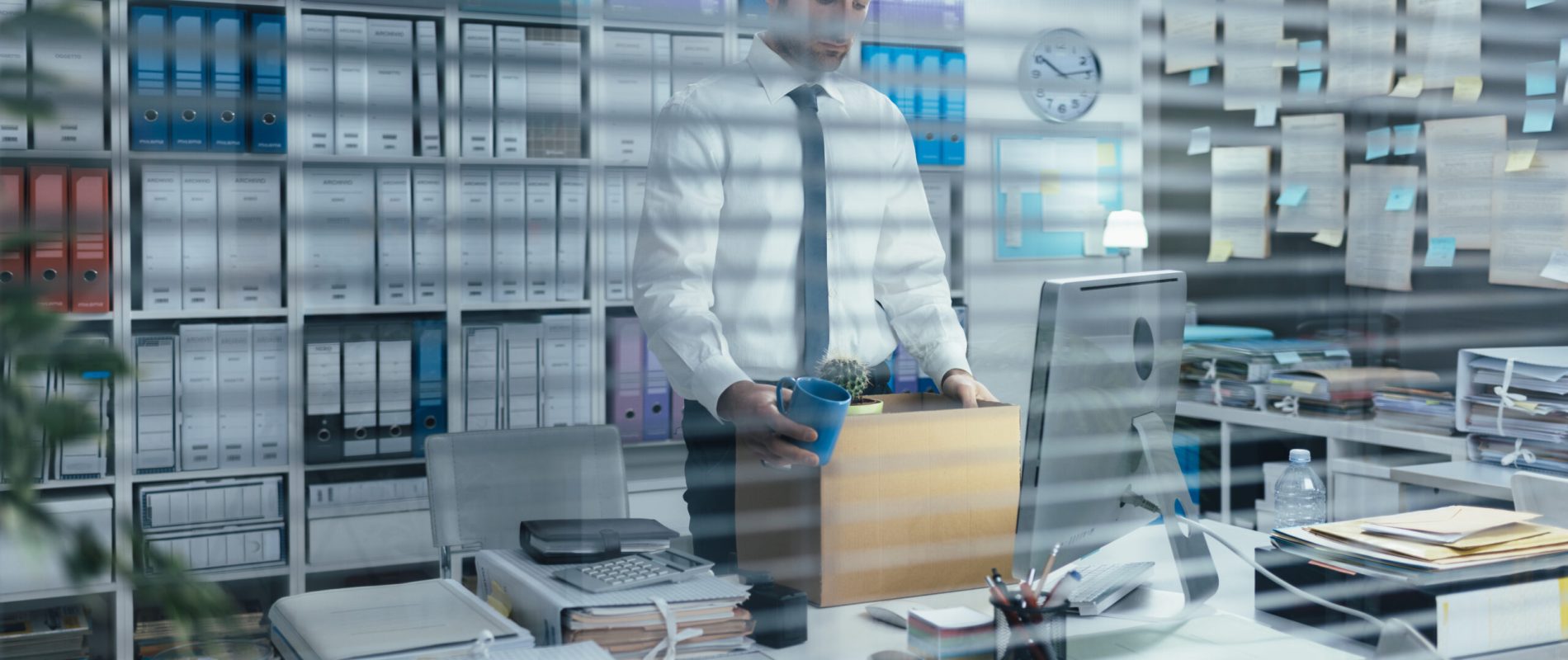 Sad office worker packing his belongings after being fired, he is holding a cardboard box