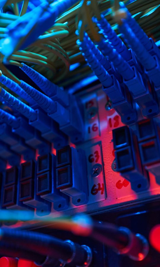 Blue optical fiber cables inserted into ports of switch panel inside server rack