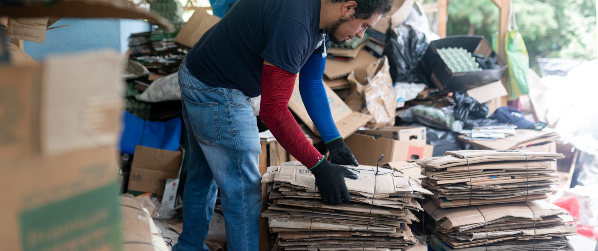 Young Hispanic man using a large-scale to weigh cardboard in a recycling plant, highlighting sustainable practices in action